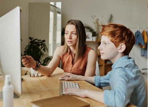 A woman and boy sitting at a table with a computer.