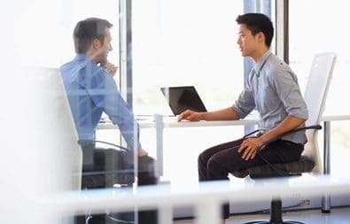 Two men sitting at a table with laptops.